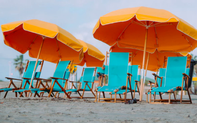 A collection of torquose beach chairs and orange umbrellas on a beach